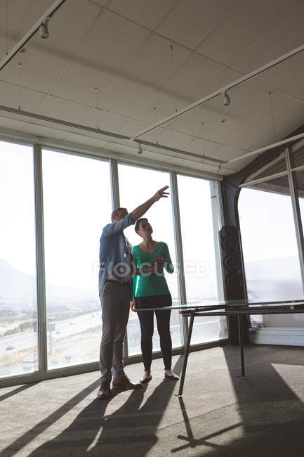 Vista de baixo ângulo dos arquitetos caucasianos assistindo o escritório enquanto discutem e seguram um tablet digital — Fotografia de Stock