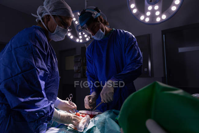 Vista lateral de cirujanos atentos realizando operación en quirófano en el hospital - foto de stock