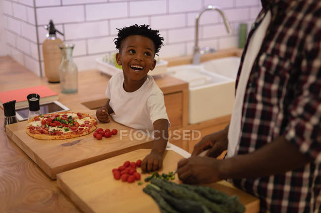 Seitenansicht des süßen afrikanisch-amerikanischen Sohnes, der seinem Vater in der heimischen Küche hilft. der Junge lächelt — Stockfoto