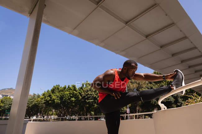 Vista laterale del giovane afro-americano in forma che fa esercizio sotto il ponte sulla ringhiera — Foto stock