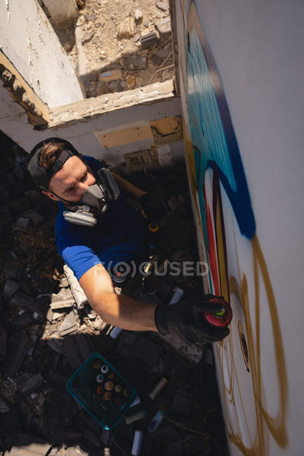 High angle view of young Caucasian graffiti artist spray painting weathered wall room — Stock Photo