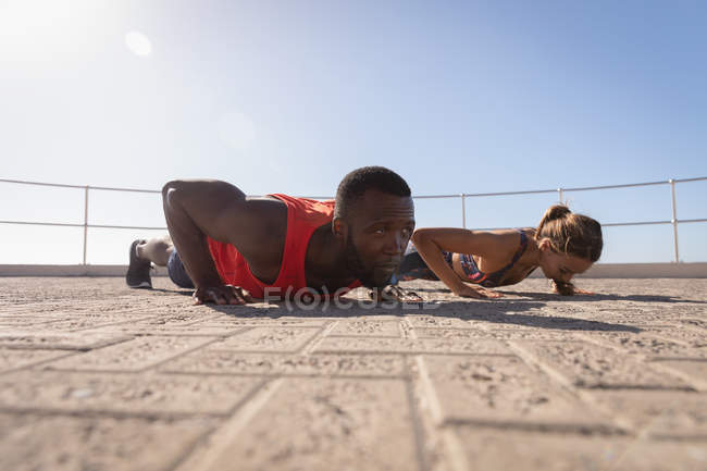 Side view of young couple doing exercise on pavement near promenade beach on sunny day — Stock Photo