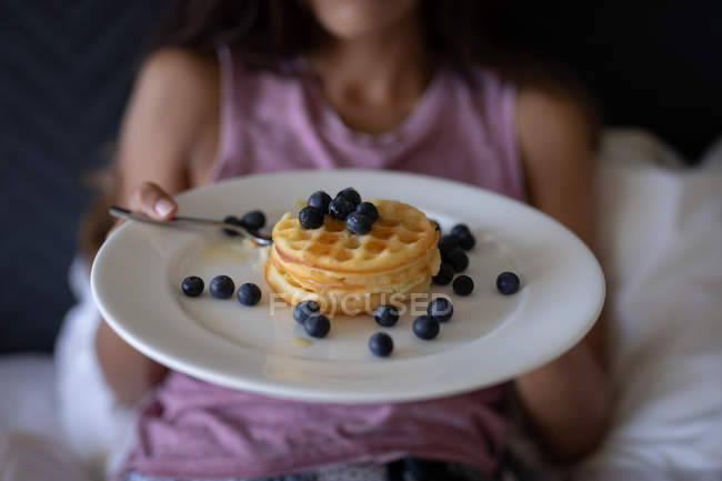 Mid section of woman holding plate of breakfast while leaning on bed at home — Stock Photo