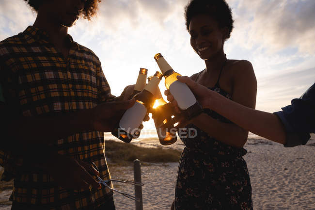 Low angle view of multi-ethnic friends group toasting beer bottle at beach in the sunshine — Stock Photo