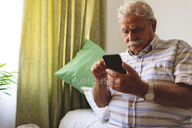 Vista frontal do homem caucasiano sênior usando telefone celular em casa de repouso — Fotografia de Stock