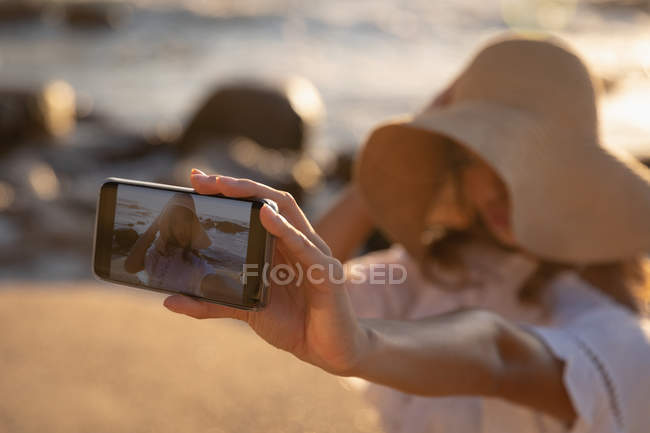 Vista lateral da mulher falando selfie na praia em um dia ensolarado — Fotografia de Stock