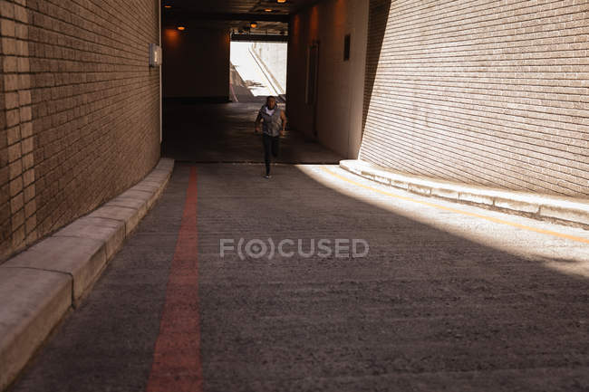 Vista frontal del joven afroamericano en forma hombre corriendo de la calle en un día soleado - foto de stock