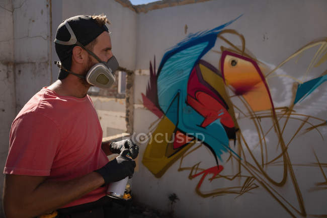 Vue latérale d'un jeune graffeur caucasien réfléchi debout devant un mur dans une ruelle — Photo de stock