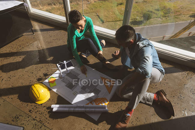 High angle view of Caucasian architects sitting on the office floor while they are examining  over a blueprint at office. They are sitting next to the window. — Stock Photo