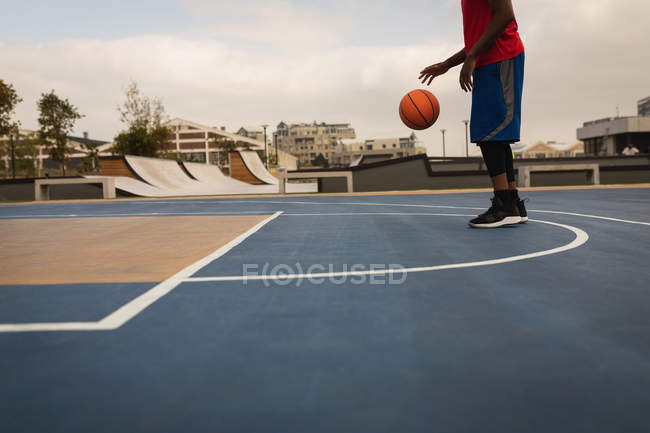 Low section of basketball player playing basketball at basketball court with a skate park in background — Stock Photo