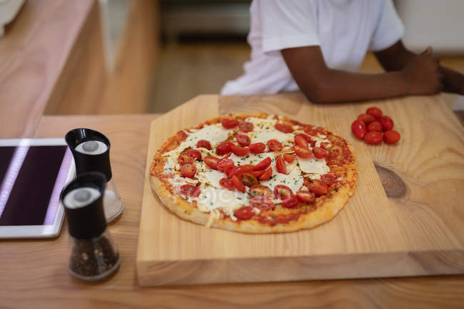 Высокий угол обзора томатной пиццы на доске для рубки на кухне дома — стоковое фото