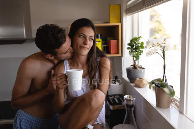 Vista frontal de pareja romántica multiétnica avergonzándose mutuamente en la cocina en casa - foto de stock