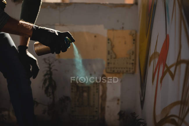 Vista laterale del giovane artista graffiti caucasico che tiene bomboletta aerosol contro la parete nel vicolo — Foto stock