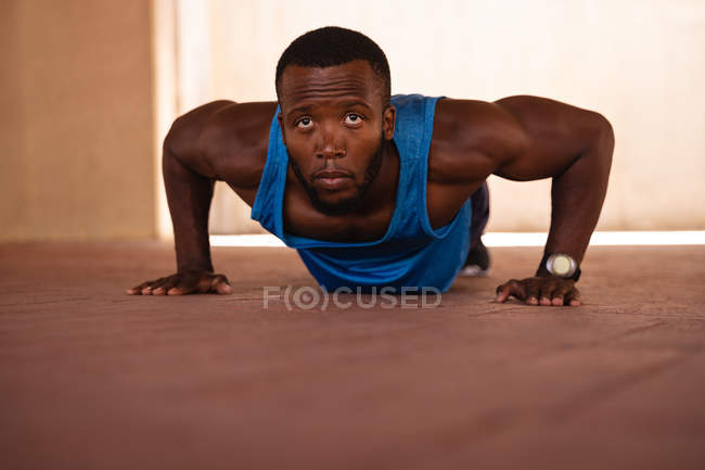 Ritratto di giovane afro-americano in forma che fa esercizio di push-up sotto il ponte. Sta guardando la telecamera. — Foto stock