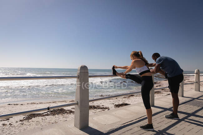 Вид сбоку молодой многонациональной пары, занимающейся спортом рядом с пляжем на набережной — стоковое фото