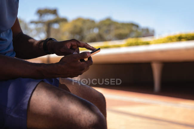 Side view of fit man using mobile phone while sitting on street side — Stock Photo