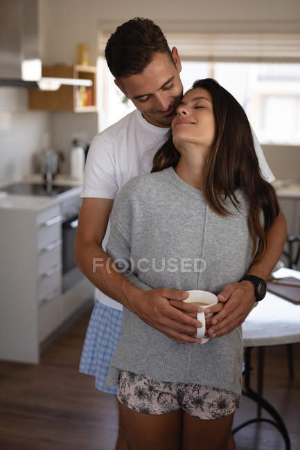 Vista frontale di romantica coppia multietnica in piedi con braccio intorno mentre si beve una tazza di caffè — Foto stock