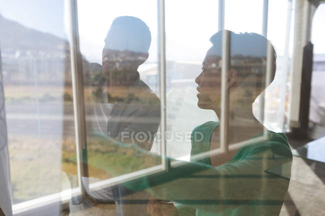 Vista frontale di architetti caucasici che tengono cianografia contro finestra e ne discutono in ufficio — Foto stock