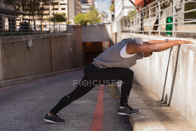 Vista lateral do homem afro-americano fazendo exercícios e se estende na rua — Fotografia de Stock