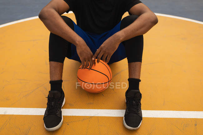 Низкая часть игрока расслабляется сидя на баскетбольной площадке — стоковое фото