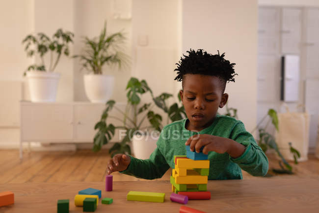 Vista frontale del piccolo ragazzo afroamericano carino che gioca con i blocchi di costruzione a casa — Foto stock