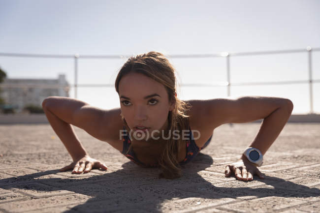 Fuente vista de la mujer haciendo flexiones en el pavimento cerca de la playa en un día soleado - foto de stock