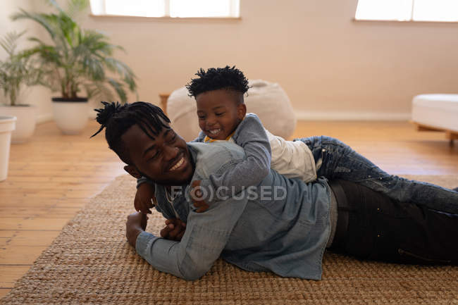 Вид збоку щасливий афро-американський батько і син під час лежав на підлозі в домашніх умовах — стокове фото
