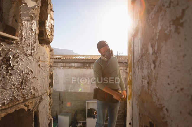 Front view of young Caucasian graffiti artist spray painting on weathered wall on sunny day — Stock Photo