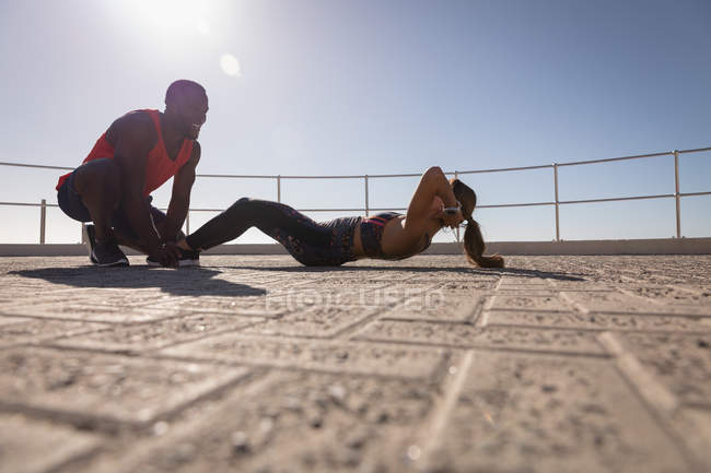 Вид сбоку афроамериканца, помогающего кавказке за хрустящие упражнения в солнечный день — стоковое фото