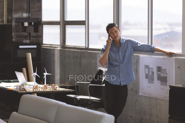 Front view of young Asian male executive talking on mobile phone in the office — Stock Photo