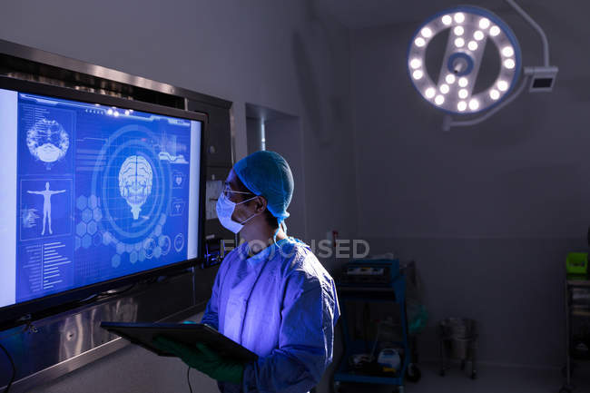 Вид збоку на чоловічий хірург, який дивиться на синій цифровий екран в операційній кімнаті в лікарні — стокове фото