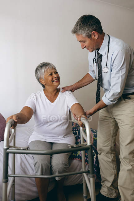 Первый взгляд на врача-кавказца, помогающего пожилой пациентке смешанной расы гулять с Уокером — стоковое фото