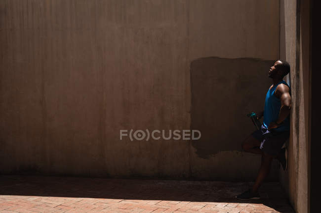 Vue latérale du jeune homme en forme afro-américain debout à côté du mur par une journée ensoleillée — Photo de stock