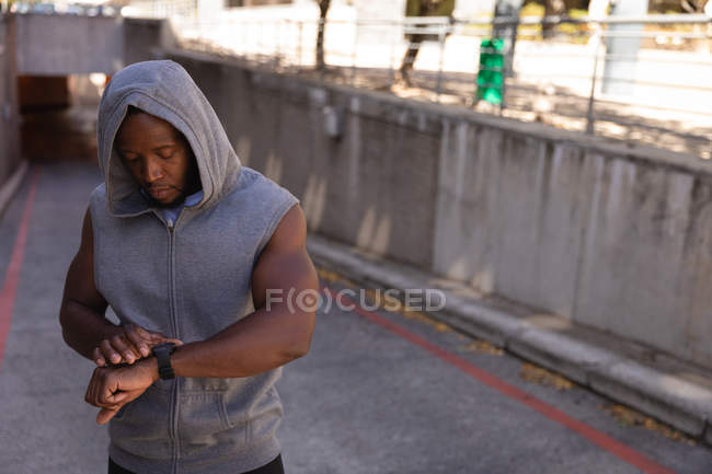 Front view of young African-American man looking at smart watch on street. Setting his swatch — Stock Photo