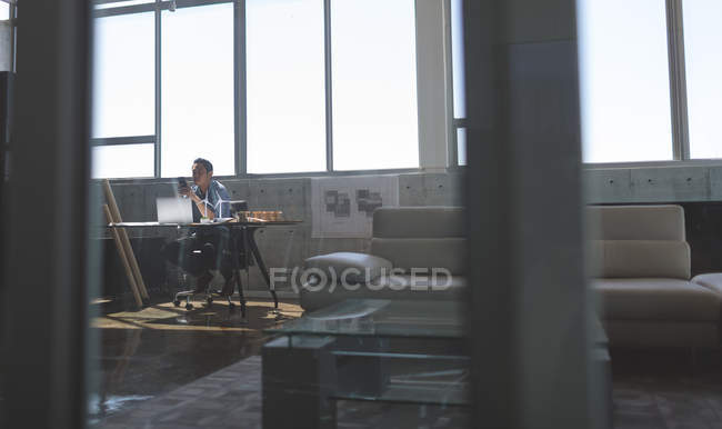 Вид азиатского архитектора-мужчины с мобильным телефоном за рабочим столом в современном офисе — стоковое фото