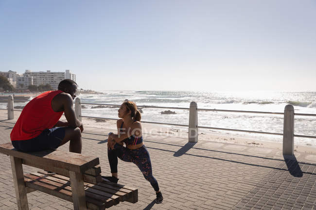 Vista frontale della giovane coppia multietnica che interagisce tra loro durante l'esercizio in spiaggia — Foto stock