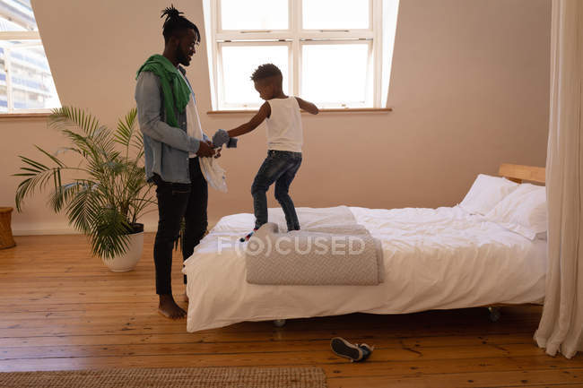 Vista lateral del apuesto padre afroamericano desnudándose hijo travieso en casa - foto de stock
