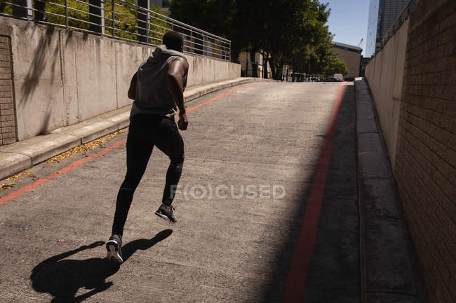 Вид сзади на молодого афроамериканца, бегущего с улицы в солнечный день — стоковое фото
