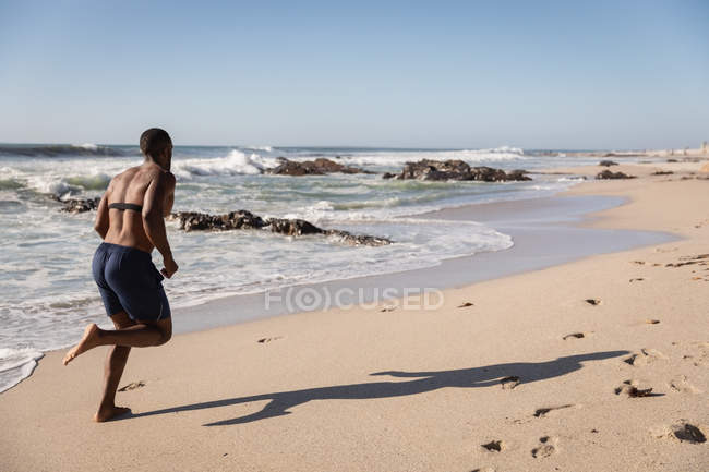 Вид на молодого афроамериканца, бегающего на пляже в солнечный день — стоковое фото