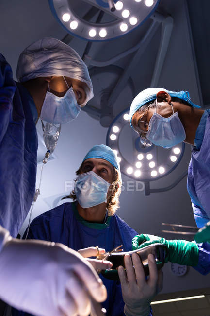 Низький кут зору багатоетнічного хірургів виконання операції в операційній в лікарні з Світильники на стелю — стокове фото