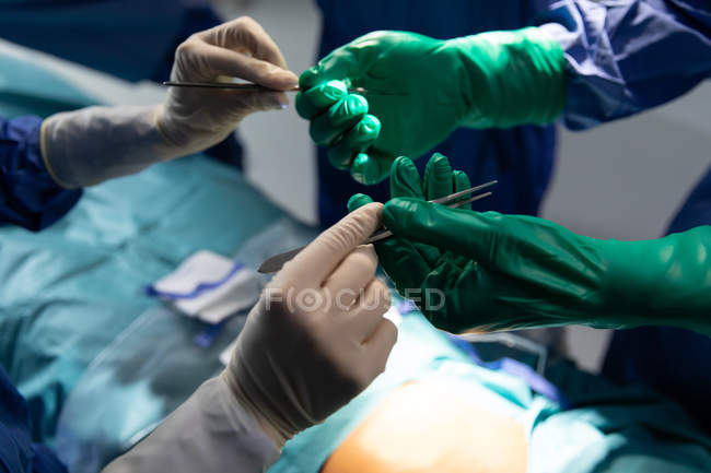 Gros plan de chirurgiens tenant un couteau chirurgical et des pinces dans la salle d'opération pendant une intervention chirurgicale à l'hôpital — Photo de stock