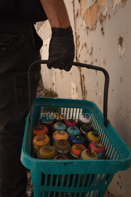 Sección media del artista de graffiti caminando con canasta de pintura en aerosol en el callejón - foto de stock