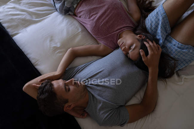 Vista de alto ângulo de casal romântico multi-étnico olhando um para o outro enquanto deitado na cama em casa — Fotografia de Stock