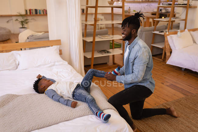 Side view of happy African-American father kneeling while dressing his son at home — Stock Photo