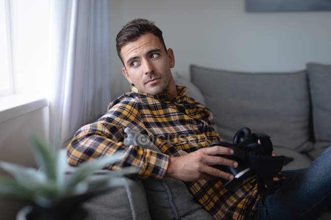 Vista frontale di un uomo caucasico premuroso con auricolare in realtà virtuale seduto sul divano a casa — Foto stock