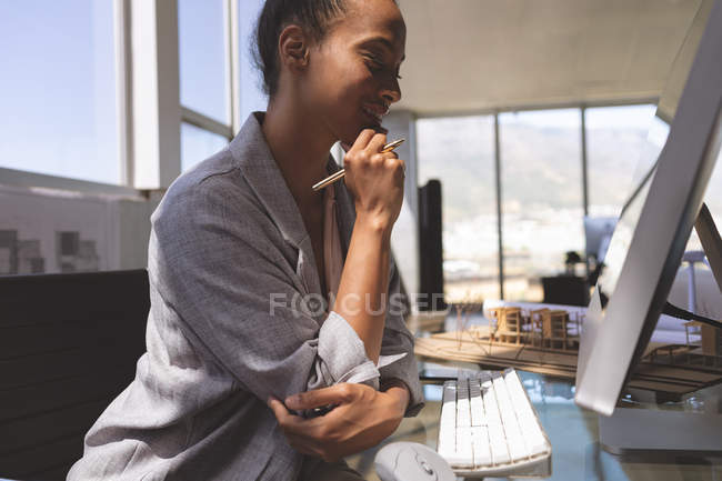 Вид збоку молодої бізнес-леді змішаної раси, що працює на комп'ютері за столом в офісі — стокове фото