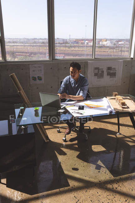 High angle view of Asian male architect sitting at desk and working on laptop in a modern office — Stock Photo