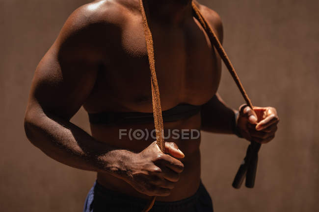 Mid section of fit man standing while holding skipping rope on shoulder — Stock Photo