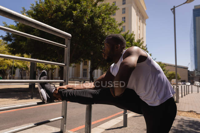Вид збоку молодий американський-африканської fit людина, роблять розтяжку вправа проти перила по вулиці — стокове фото