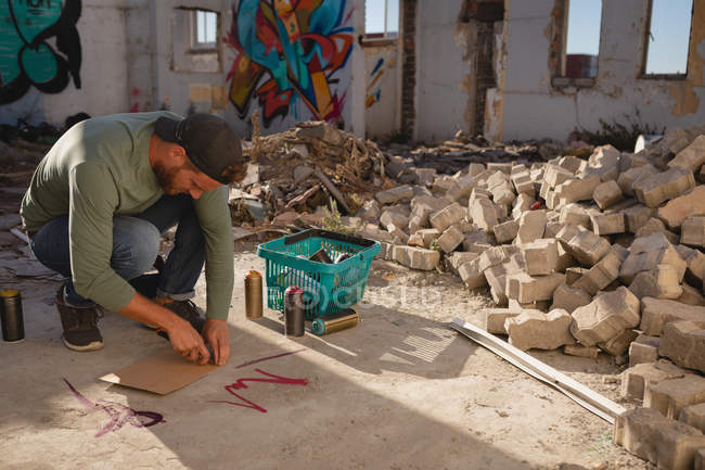 Vista lateral del joven artista de graffiti caucásico dibujando en cartón marcador de ingenio en la calle - foto de stock